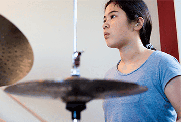 A female musician with hearing aids plays a drum set in the St. Louis, MO area.